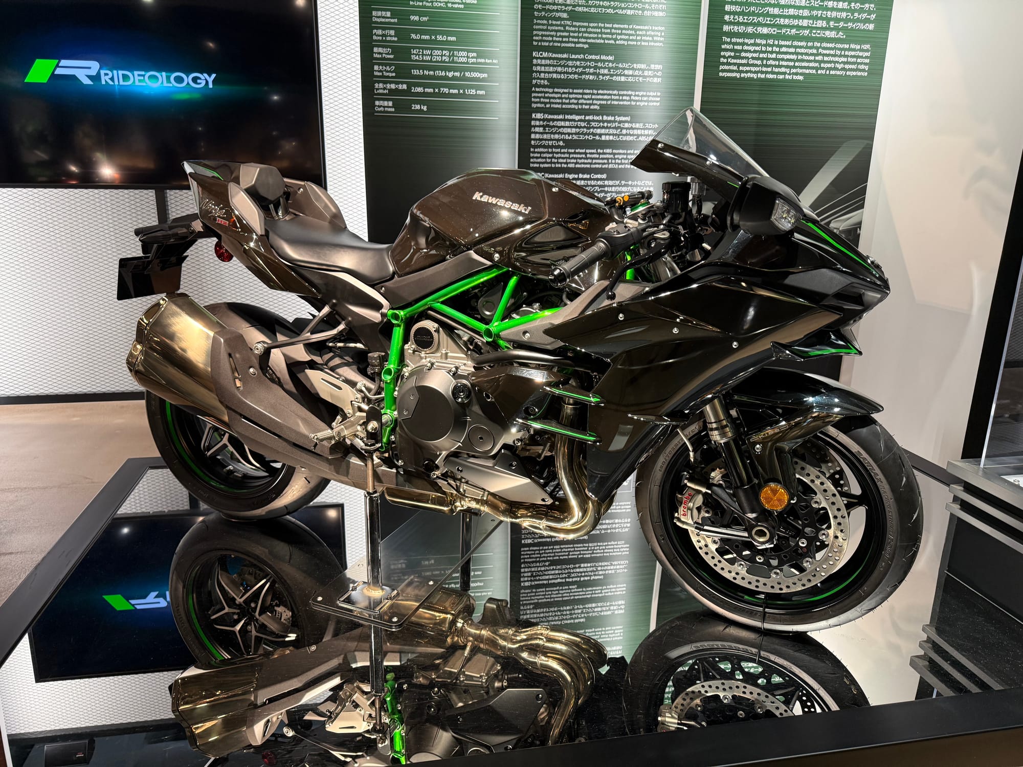 Kawasaki Ninja H2 motorcycle displayed at Kawasaki Good Times World in Kobe, featuring a supercharged engine, black bodywork, green trellis frame and aerodynamic styling.