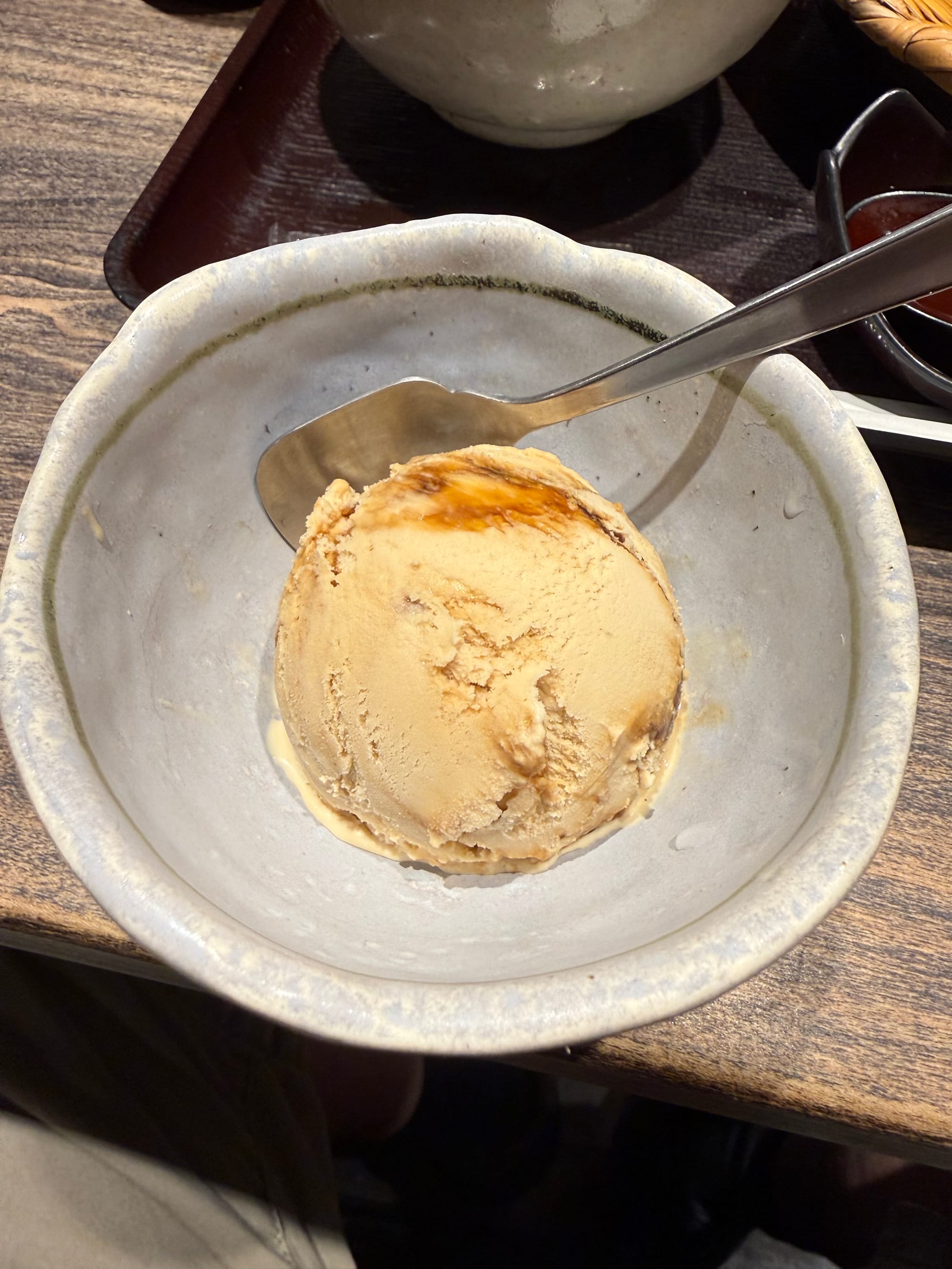 Scoop of Okinawa brown sugar ice cream served in a ceramic bowl, showing caramel-coloured swirls and a smooth texture, with a spoon resting beside the dessert.