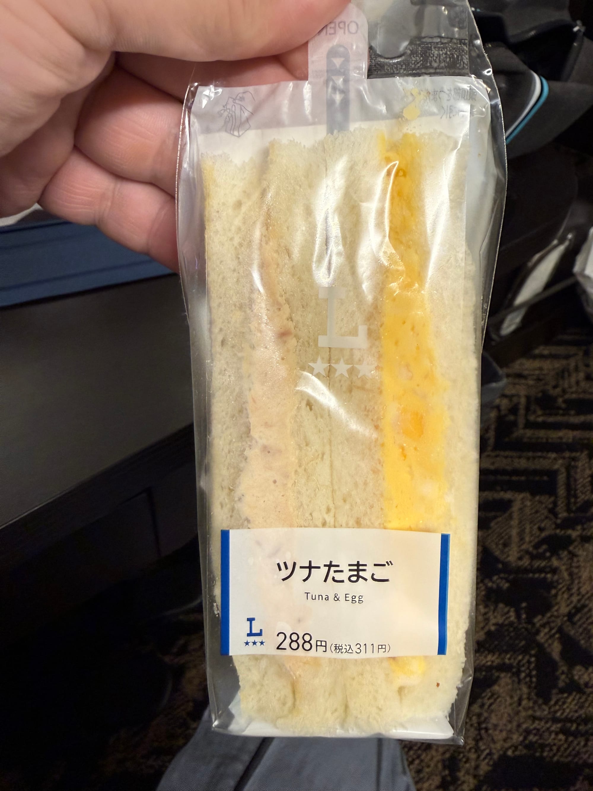 Lawson convenience store tuna and egg sandwich in retail packaging, showing soft white bread filled with tuna mayonnaise and chopped boiled egg, with Japanese and English labelling.