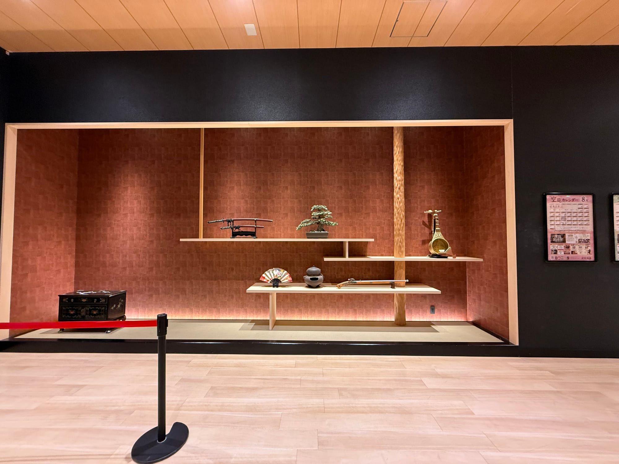 Traditional Japanese decorative alcove at Solaniwa Onsen Osaka Bay Tower, displaying samurai swords, a bonsai, a folding fan and other cultural artefacts against a red backdrop.