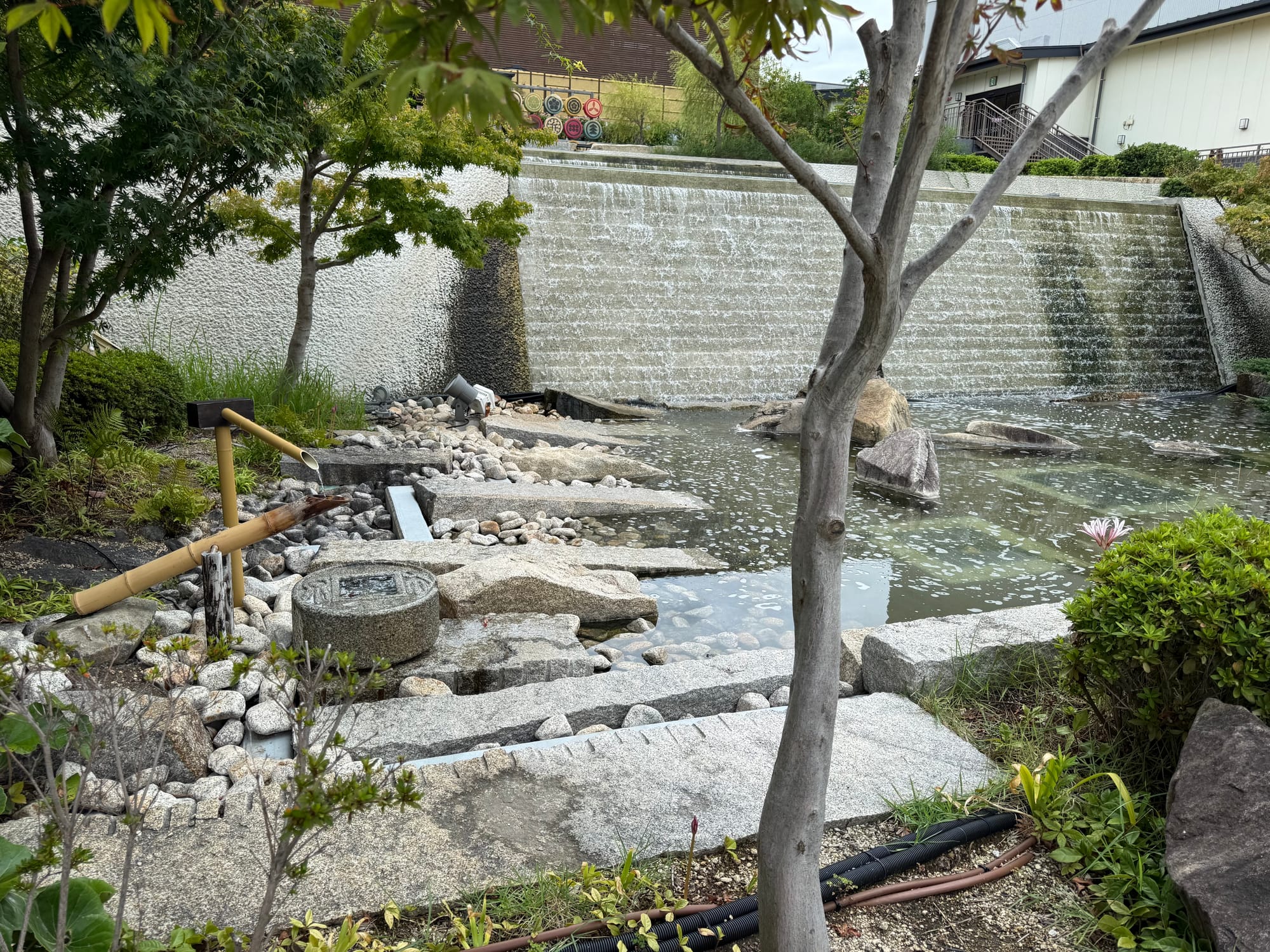 Japanese-style garden at Solaniwa Onsen Osaka Bay Tower, featuring a pond, waterfall, stone pathways, bamboo water spout and landscaped greenery within the rooftop grounds.