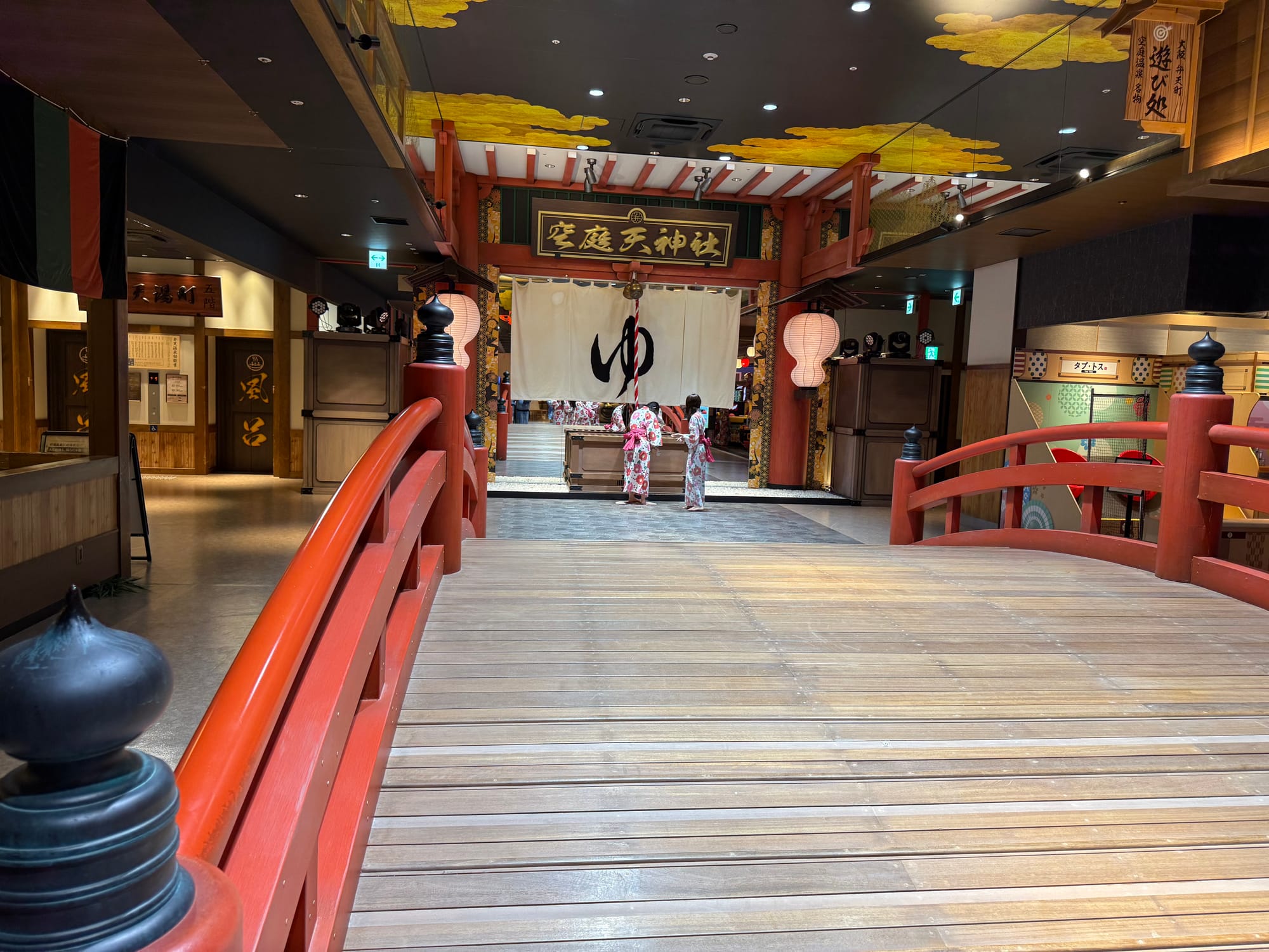 Traditional Japanese-style interior at Solaniwa Onsen Osaka Bay Tower, featuring a red arched bridge leading to an indoor shrine decorated with lanterns, banners and ornate architecture.
