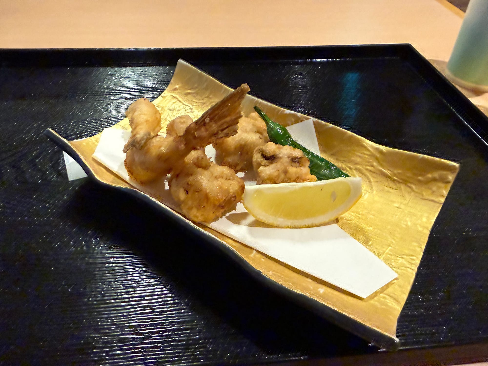 Deep-fried fugu served on a gold-coloured dish, featuring lightly battered pieces of pufferfish with a lemon wedge and green pepper garnish at a Japanese restaurant.