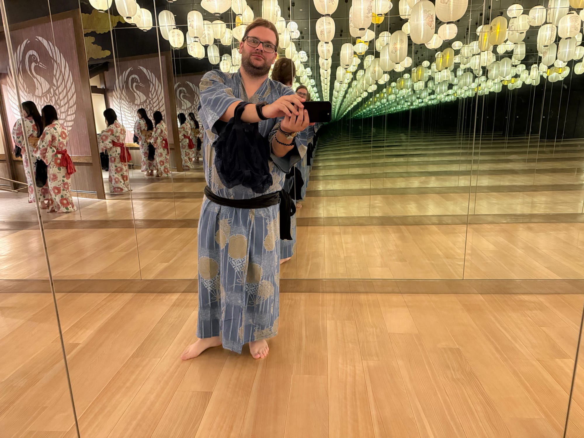 Visitor in a blue yukata taking a mirror selfie beneath rows of illuminated lanterns at Solaniwa Onsen Osaka Bay Tower, with mirrors creating an infinity-room effect.