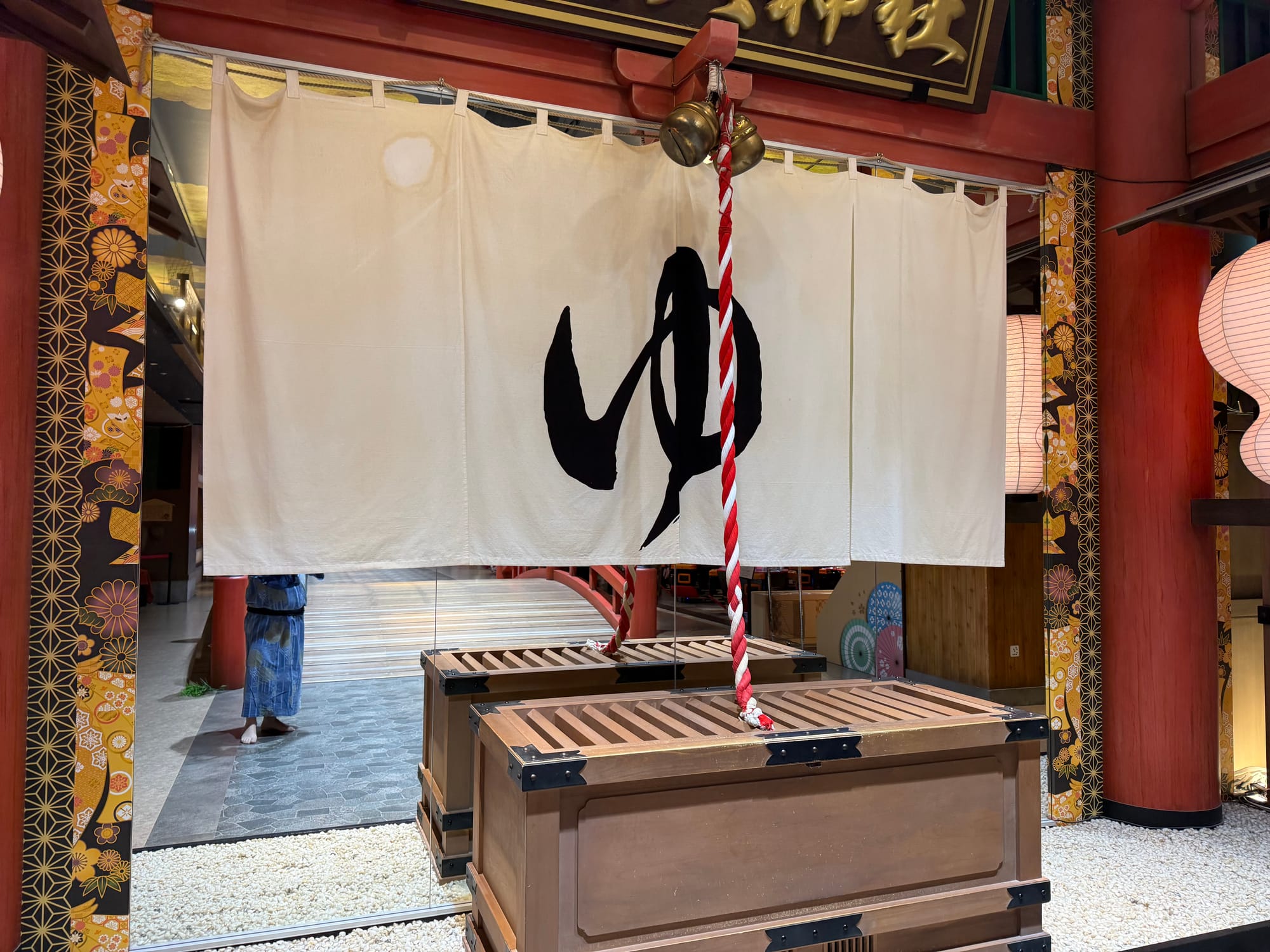 Indoor shrine at Solaniwa Onsen Osaka Bay Tower, featuring a traditional offertory box, bell rope and noren curtain marked with the Japanese character for hot water.