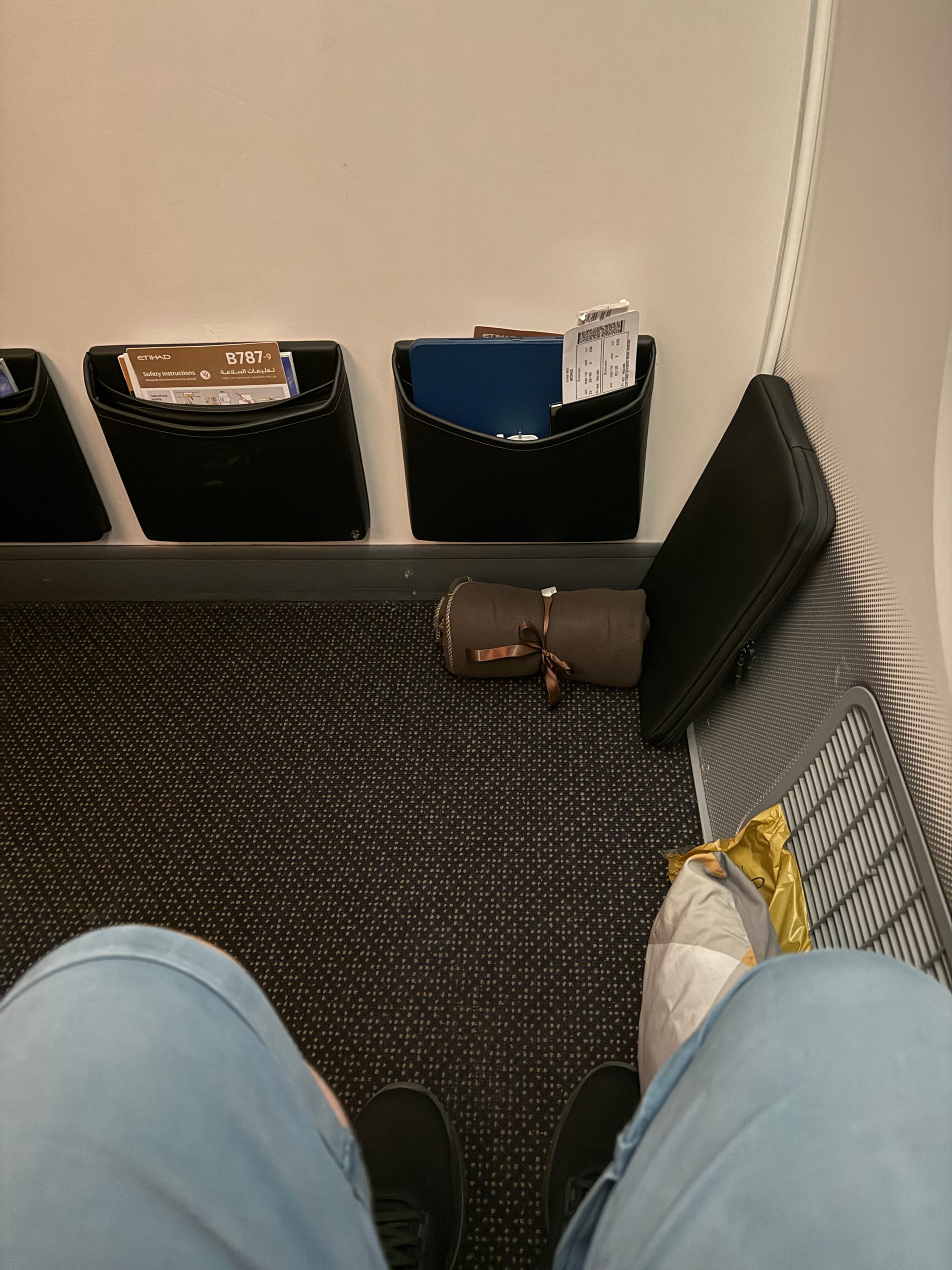 Extra-legroom Premium Economy seat on an Etihad Airways Boeing 787-9, showing the spacious bulkhead row with a pillow, blanket and personal items placed in front.