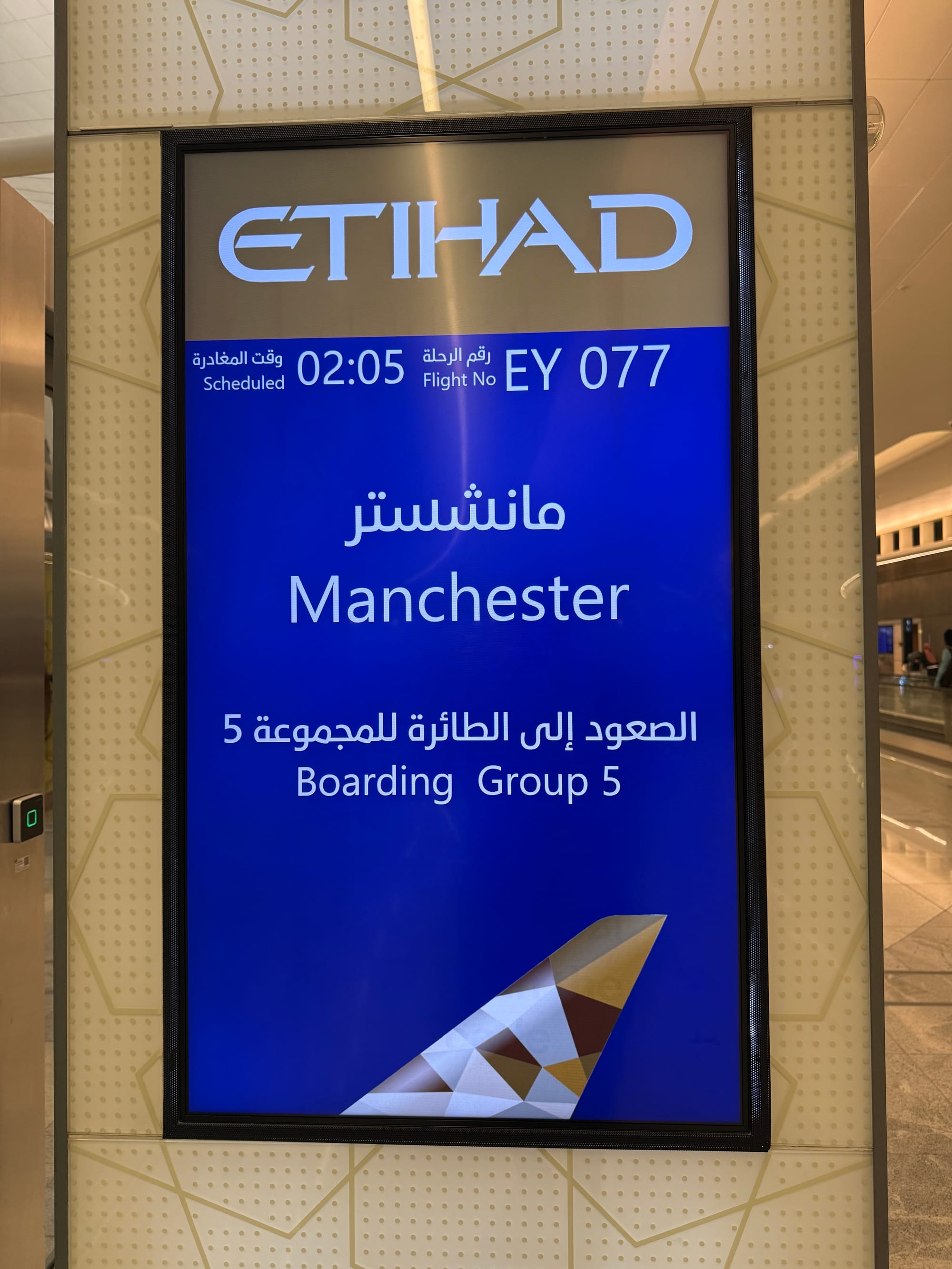 Etihad Airways flight information display at Abu Dhabi International Airport, showing flight EY077 to Manchester with boarding in progress for Group 5.