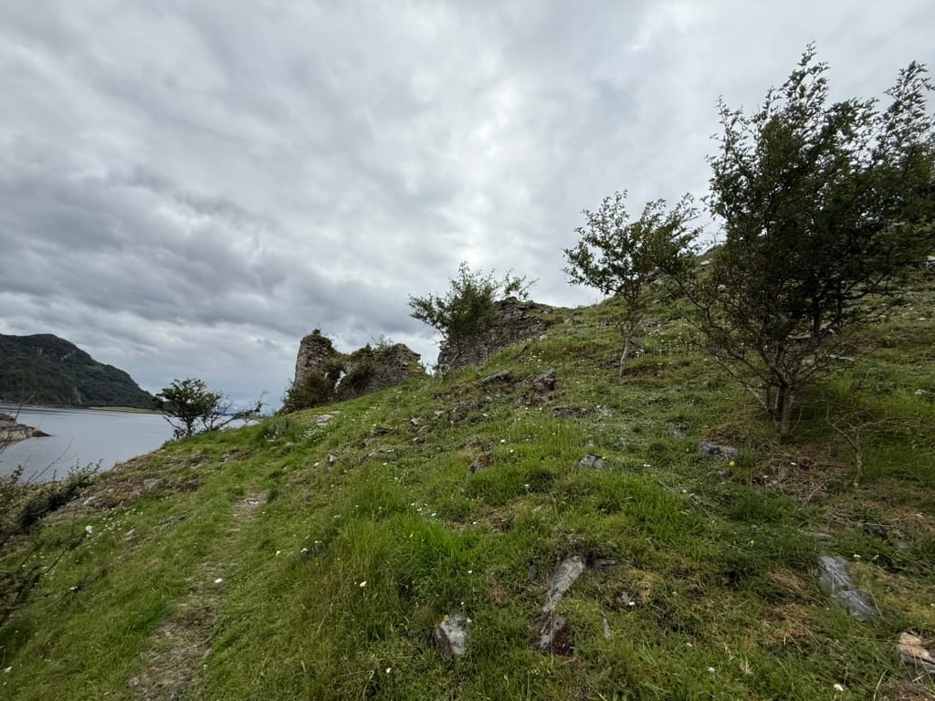 Ruined stone walls on a hillside above a Scottish loch.