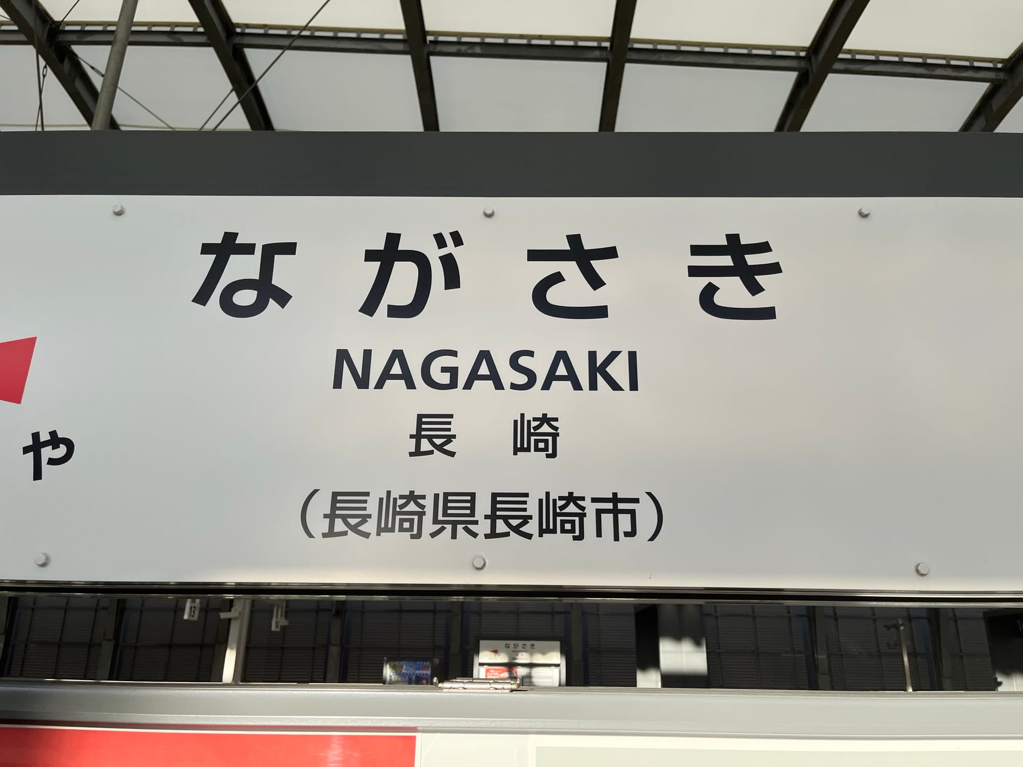 Nagasaki Station sign displaying the station name in Japanese and English, with additional location information visible on a platform within the railway station.