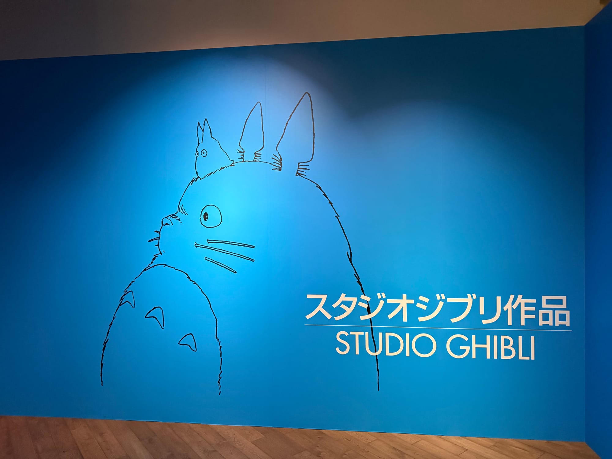 Studio Ghibli display inside Ghibli Park's Grand Warehouse, featuring a line-art illustration of Totoro and the Studio Ghibli name in Japanese and English on a blue wall.
