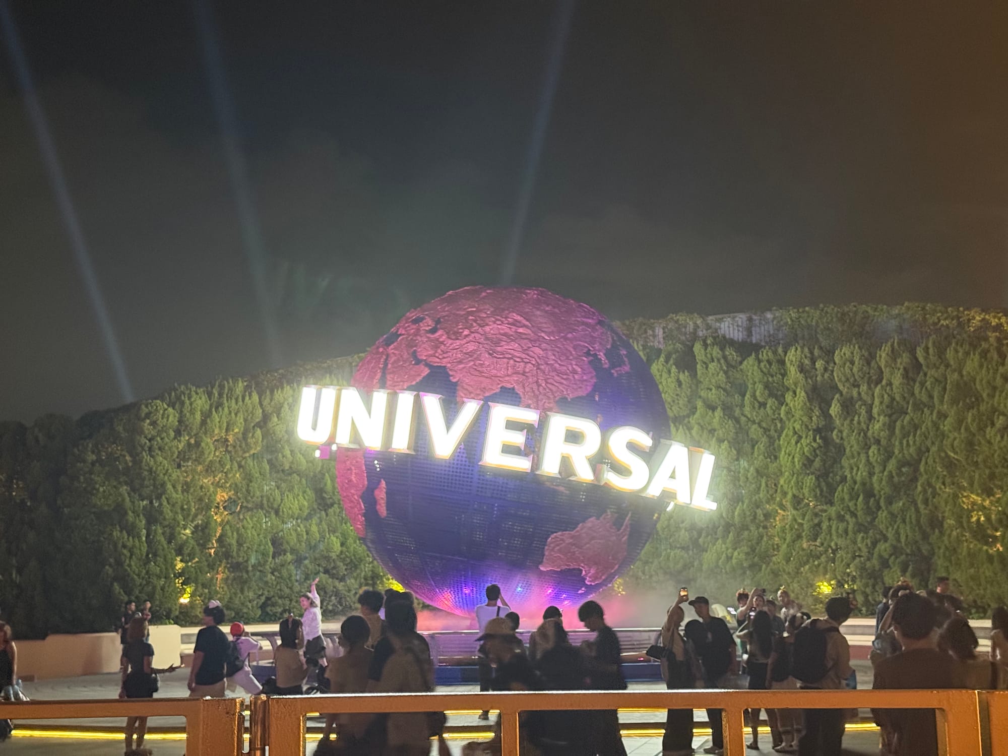 Universal Studios globe illuminated at night at Universal Studios Japan in Osaka, with visitors gathered around the iconic rotating landmark and searchlights shining overhead.
