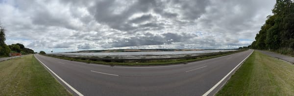 Panoramic view of the Beauly Firth beside a single carriageway under dramatic clouds.