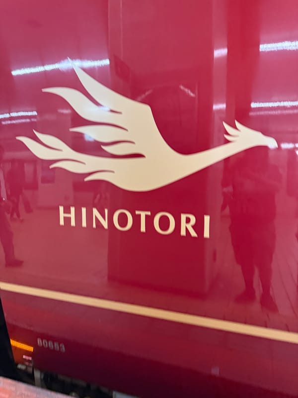 Close-up of a Kintetsu Hinotori limited express train, showing the gold phoenix logo and "HINOTORI" name on the train's distinctive deep red bodywork.