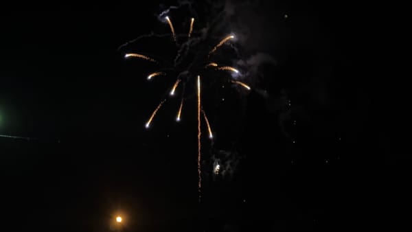 Firework bursting over Lake Suwa at night, with golden trails radiating across the dark sky and smoke illuminated by the bright display above the waterfront.