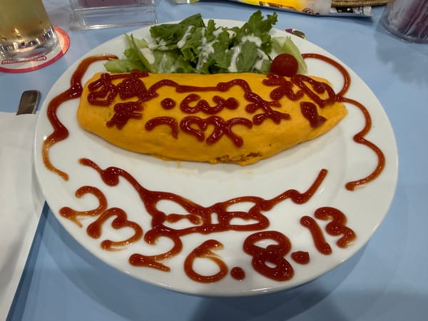 Omurice served at maidreamin Namba in Osaka, decorated with ketchup artwork of a Sanrio-style character, alongside a small salad and handwritten date on the plate.